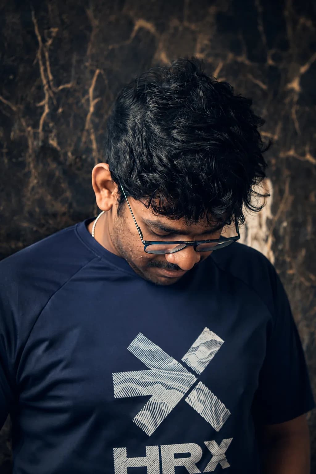A person looking downward outdoors at night, framed against a dark urban background.