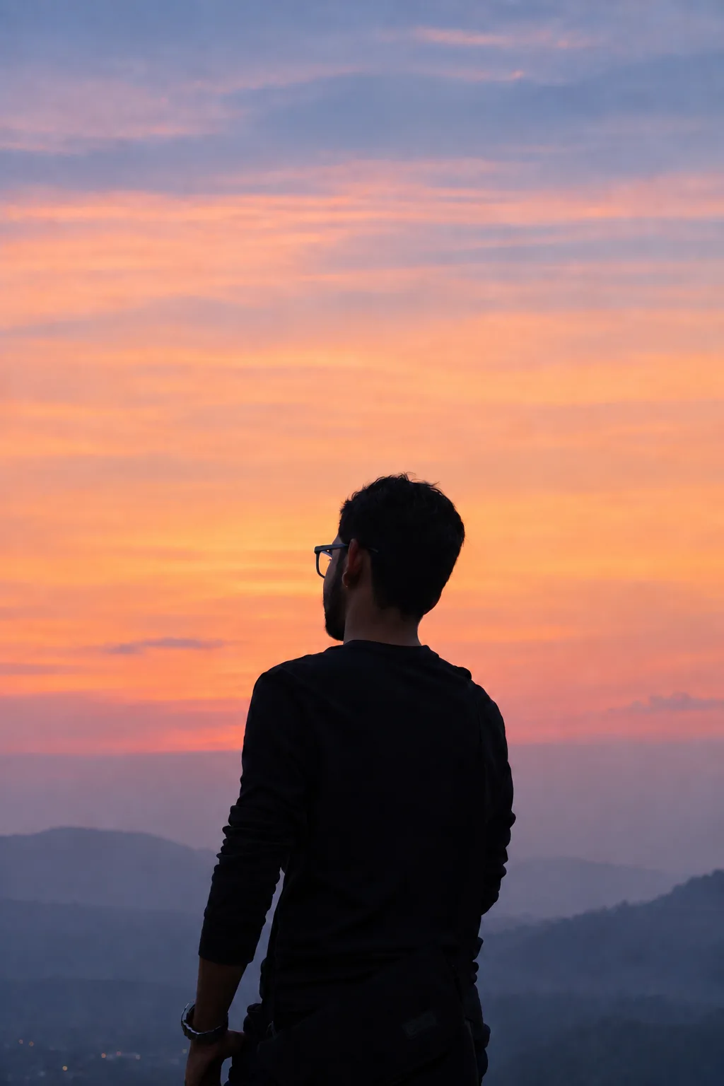 A person standing in silhouette against a pastel sunset over a mountainous landscape.
